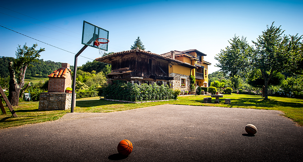 Cancha de Baloncesto y jardín con el hórreo y la casa al fondo